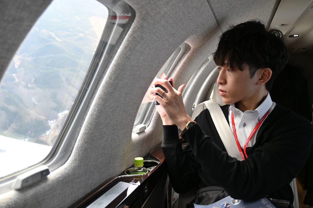 ビジネスジェット機から眼下の被災地をスマートフォンで撮影する塚田康太さん＝１６日午後３時半ごろ、石川県輪島市上空