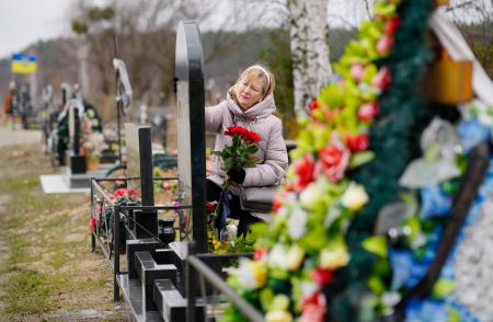 多数の市民が虐殺されたキーウ近郊ブチャにある墓地を訪れ、夫の遺影に手を伸ばすリュドミラ・キジロワさん（６９）。夫は２０２２年３月、自宅庭でロシア軍に射殺された。「夫を亡くした痛みは今後も決して消えることはない」と悲しみに耐えるように話した＝２３日（共同）