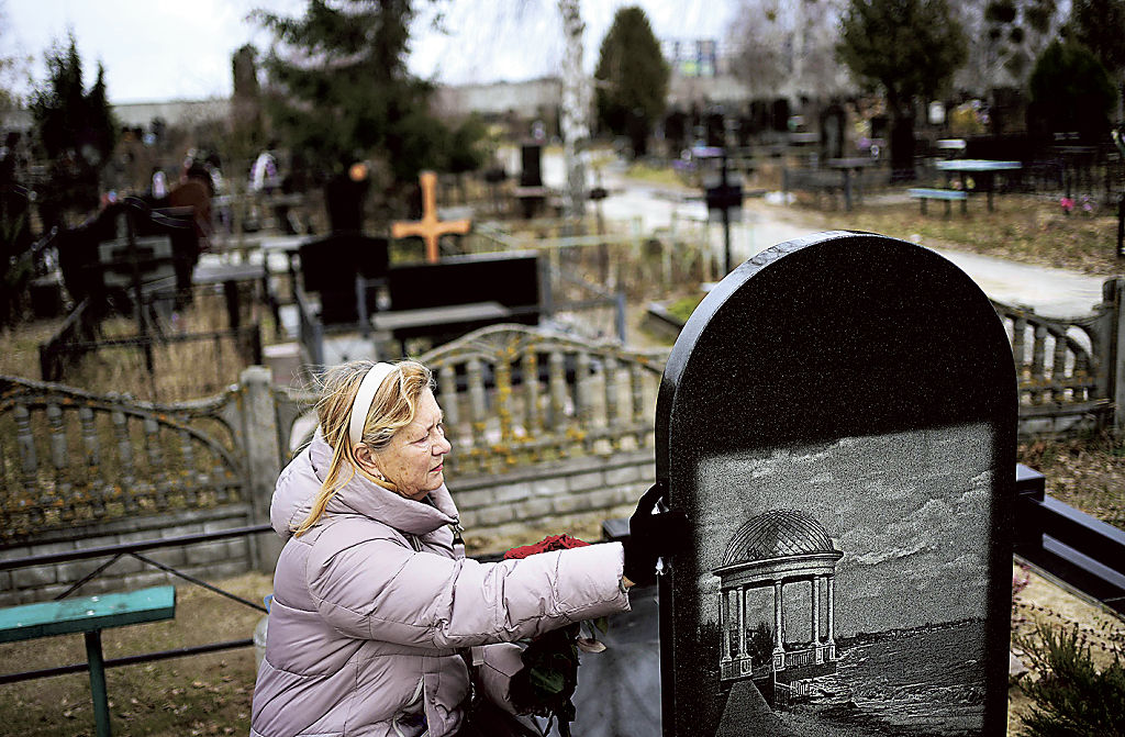 多数の市民が虐殺されたキーウ近郊ブチャにある墓地を訪れ、夫の遺影に手を伸ばすリュドミラ・キジロワさん（６９）。夫は２０２２年３月、自宅庭でロシア軍に射殺された＝２３日（共同）