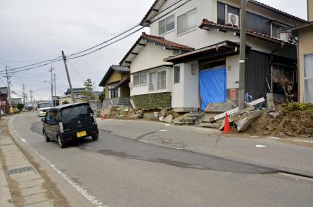 液状化とみられる現象で被害を受けた住宅と傾いた道路＝２月、石川県内灘町