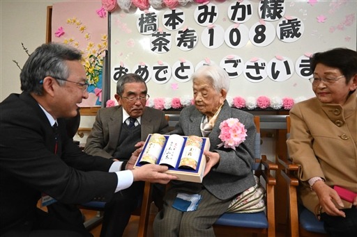 山川副区長（左）からお茶を贈られた橋本さん＝静岡市駿河区の「ハートフルホーム八幡」