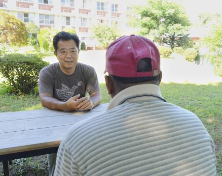 庭で談笑する有川憲治事務局長（左）とリビさん＝２０２３年８月、神奈川県鎌倉市のアルペなんみんセンター
