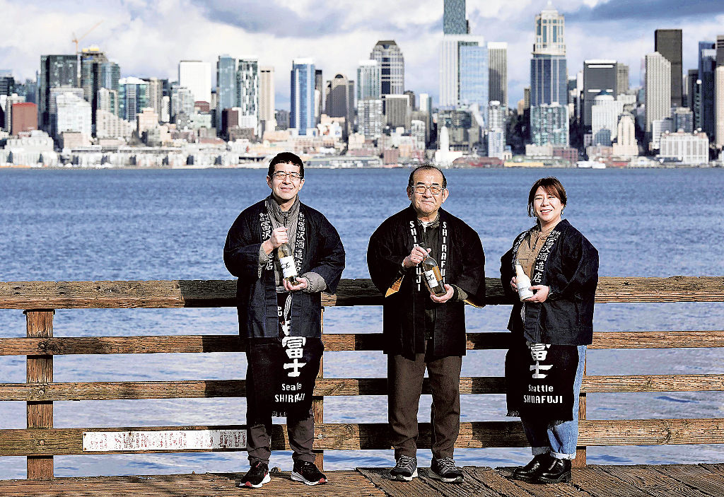 シアトルの街を背景に写真に納まる冨沢周平さん（中央）、守さん（左）、真理さん。２０２２年に米国で酒蔵を再開した。「シアトルの地酒になります」と語る＝２月、米ワシントン州（共同）