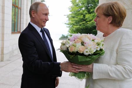 ２０１８年５月、ロシア南部ソチで、ドイツのメルケル首相（右）との会談前に花を贈ったロシアのプーチン大統領（タス＝共同）