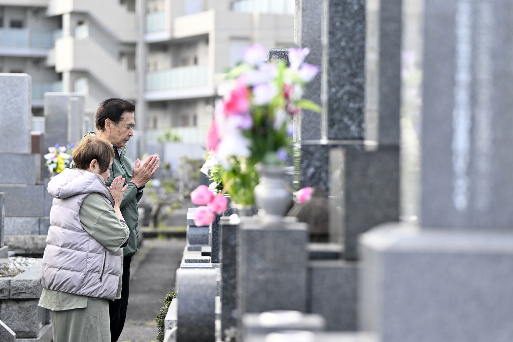 墓前で静かに手を合わせる人たち＝１７日午前、静岡市葵区の愛宕霊園