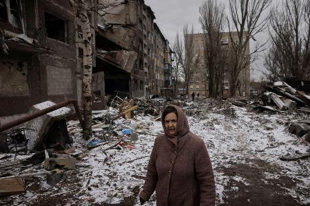ロシアのミサイル攻撃で破壊された集合住宅の横を歩く女性＝２月、ウクライナ東部