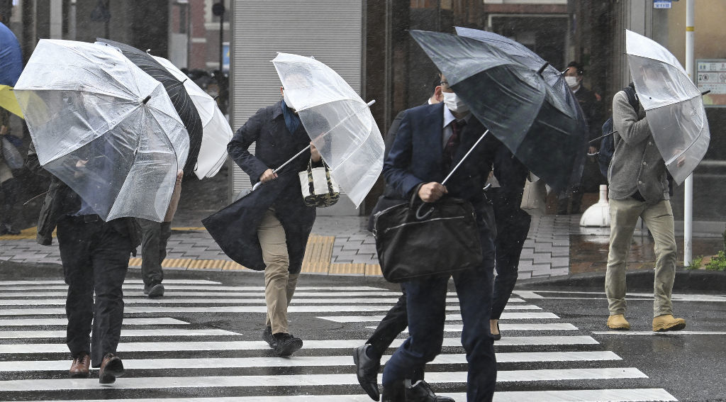 激しい風雨に傘を押さえて歩く通勤者ら＝２９日午前８時３４分、静岡市葵区