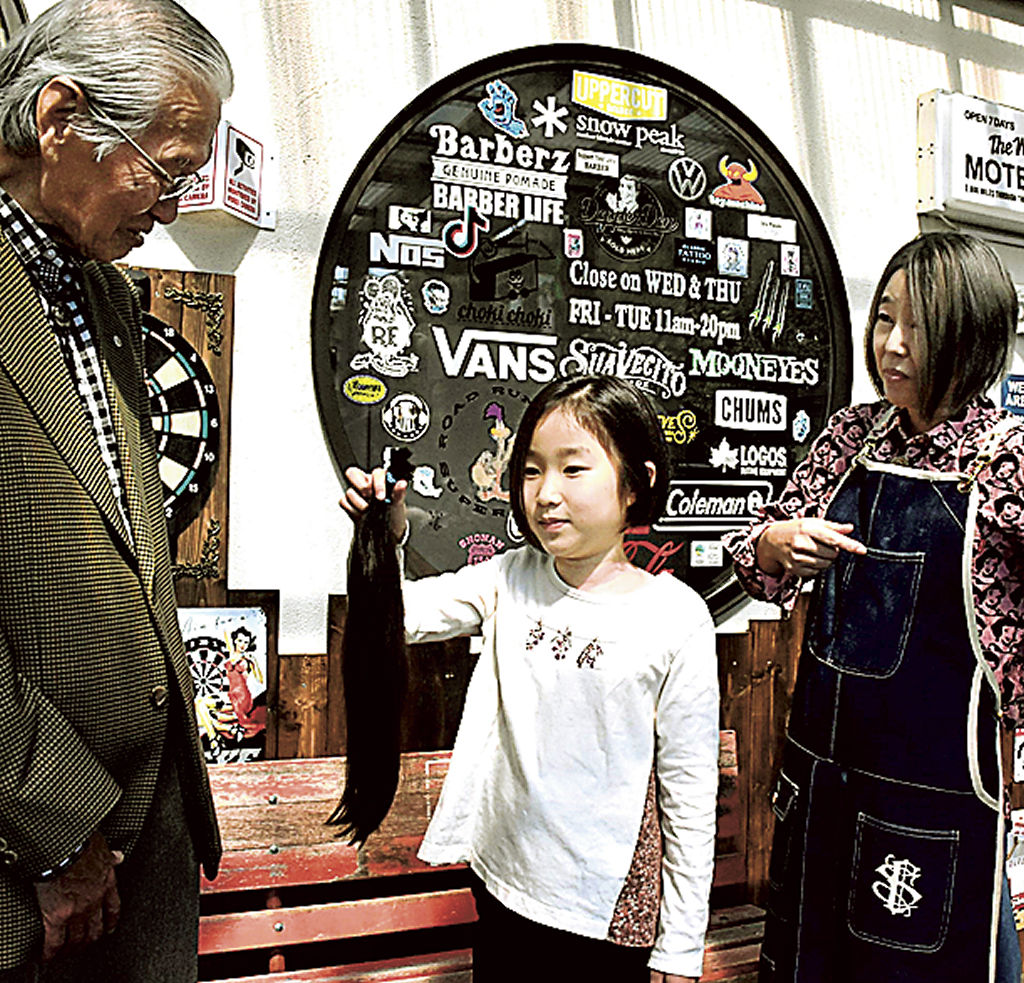 延べ１００人目の提供者となった飯田さん（中央）から髪を受け取る土屋さん（左）＝函南町のカットハウス　チョキチョキ