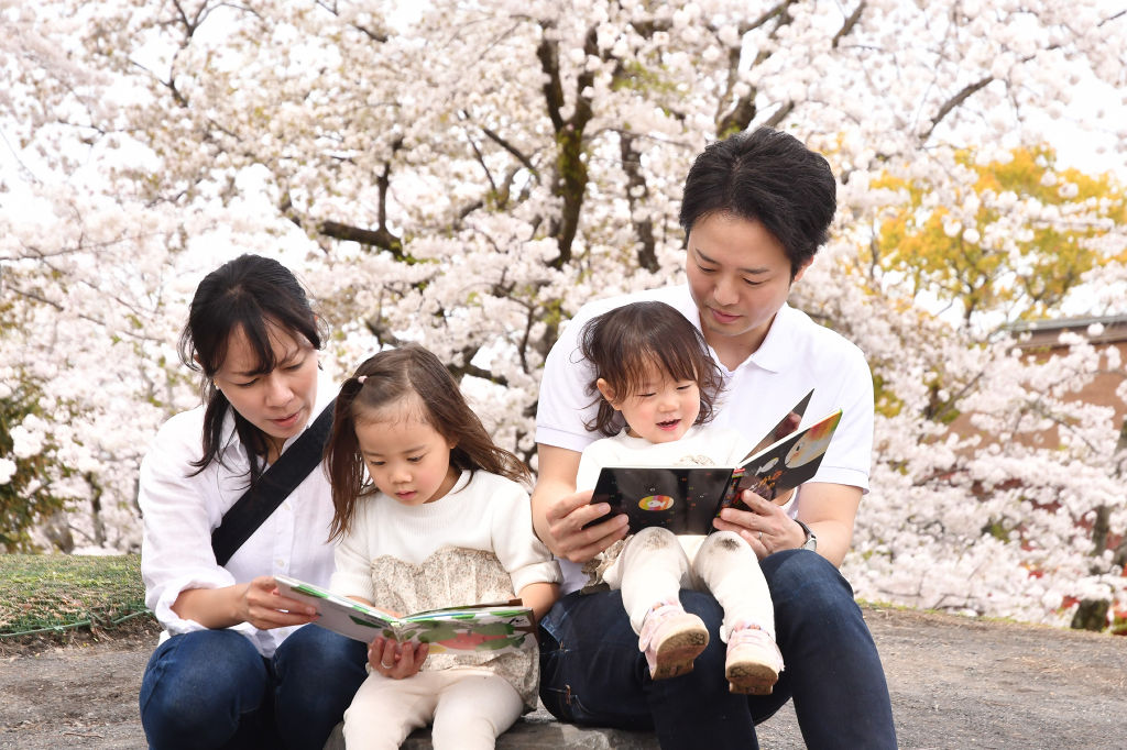 桜の木の下で読書を楽しむ家族＝富士宮市の神田川ふれあい広場