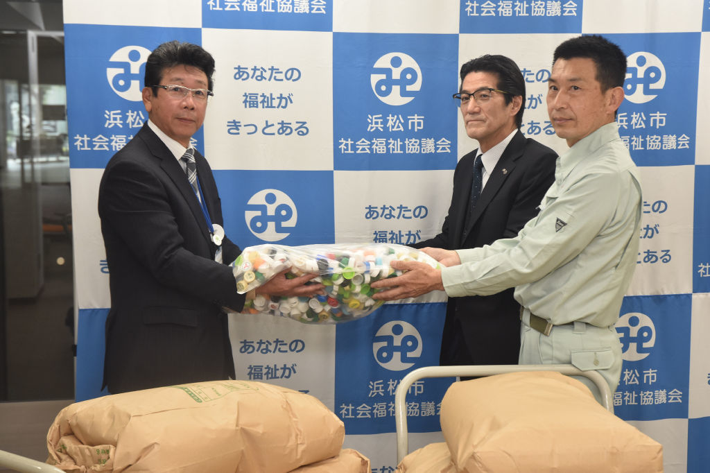 芳田浜松地区センター長（左）にキャップと米を寄贈する小沢社長（中央）ら＝浜松市中央区
