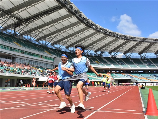２人一組の「デカパン競走」で息を合わせて走る生徒＝１３日午前、袋井市のエコパスタジアム