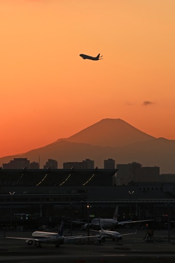 夕焼けの空に浮かび上がった富士山。羽田空港を飛び立った航空機のシルエットを捉 えた。手前は稼働が極端に減った国際線のターミナル＝５日、東京都大田区