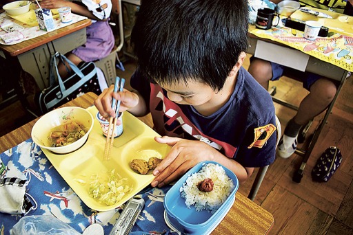 おかずの入ったトレーの横に白飯の入った弁当箱を置き、給食を食べる児童＝浜松市内