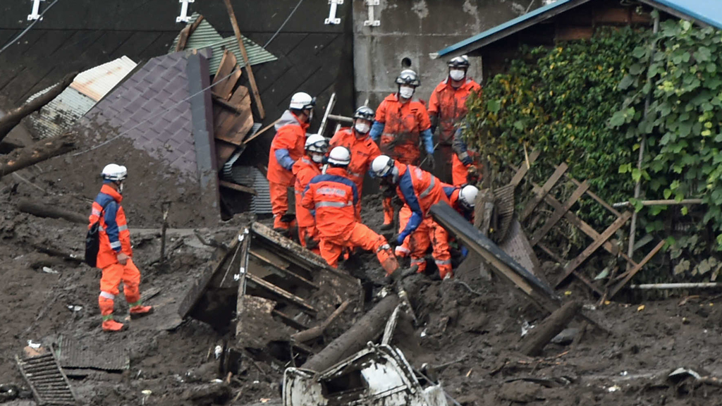 被害を受けた建物から泥やがれきなどを運び出す捜索隊員=9日午後、熱海市伊豆山