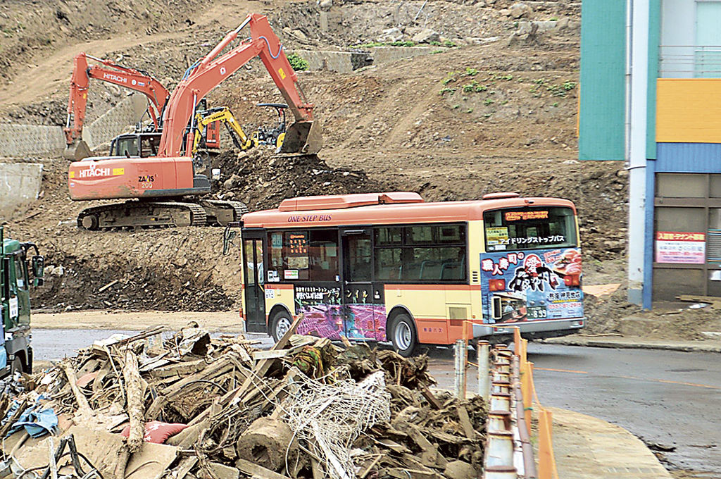 土砂やがれきが積み上がった被災地を走る路線バス＝１日午前、熱海市伊豆山