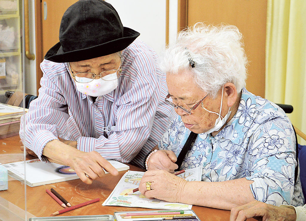生徒の隣に寄り添いながら、色の塗り方を伝える大村さん（左）＝静岡市葵区のデイサービス「亀寿庵」